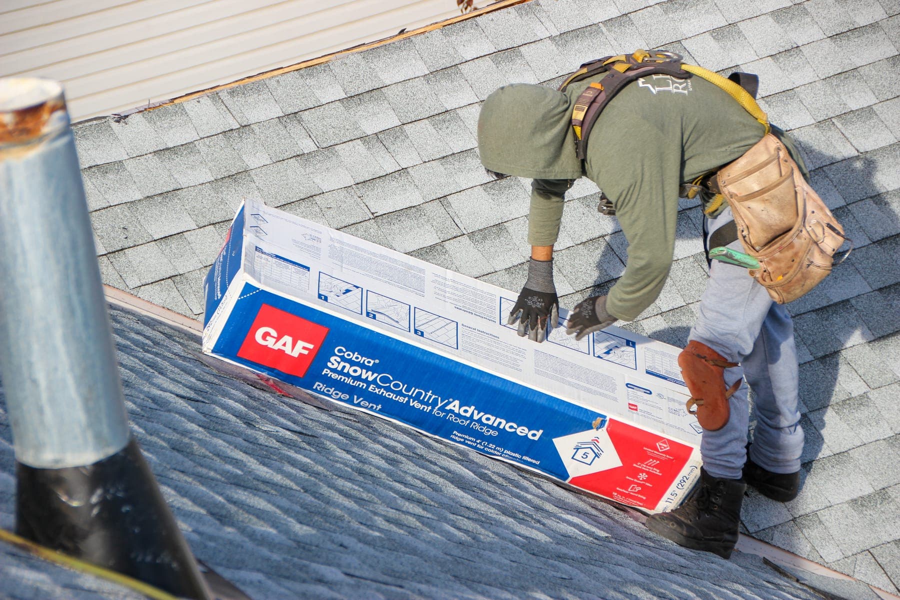 Harnessed Legacy Roofing installer placing a GAF ridge vent on a shingle roof